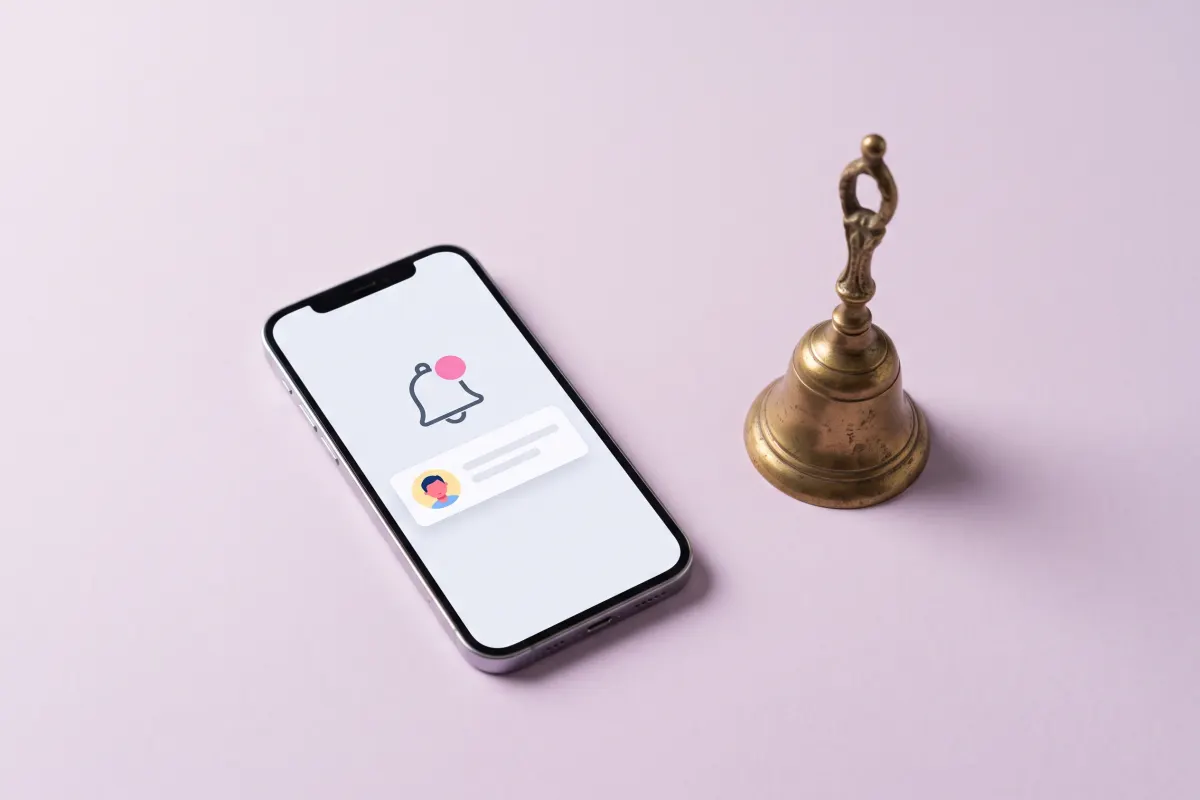 Phone with a notification bell and alert card next to a small brass bell: real-time alerts