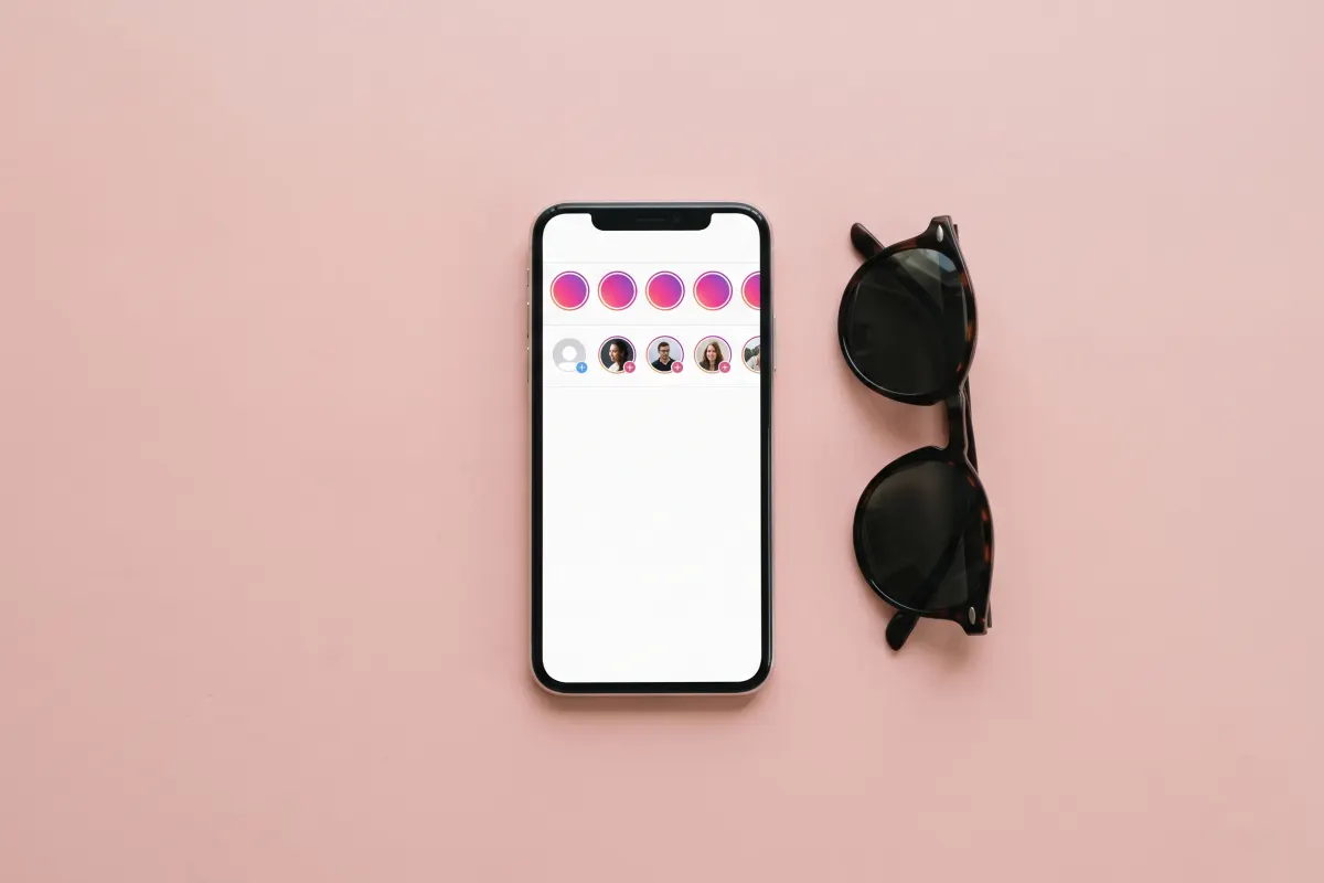 Phone showing a row of story circles and a follow timeline, next to folded sunglasses